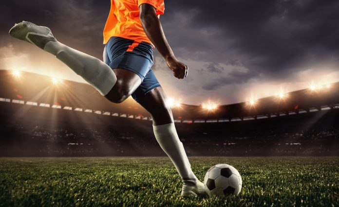 Cropped male soccer, football player kicking ball at the stadium during sport match on dark sky background.